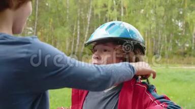 哥哥在夏天公园里把自行车头盔戴在弟弟的头上。 帮小男孩的大哥哥
